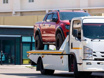 Ein rotes Pickup wird in einer sonnigen städtischen Umgebung auf einen weißen Abschleppwagen von Unfallwagenankauf Nettetal verladen.